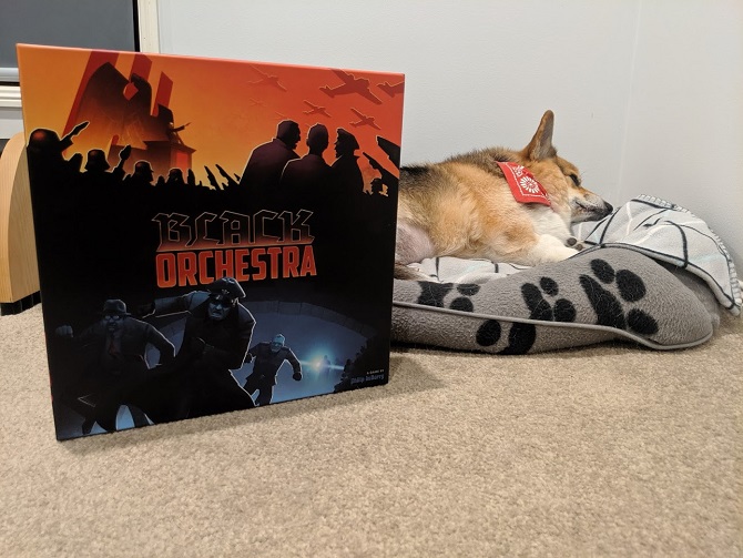 Black Orchestra box next to a sleeping corgi. It's pretty cute.