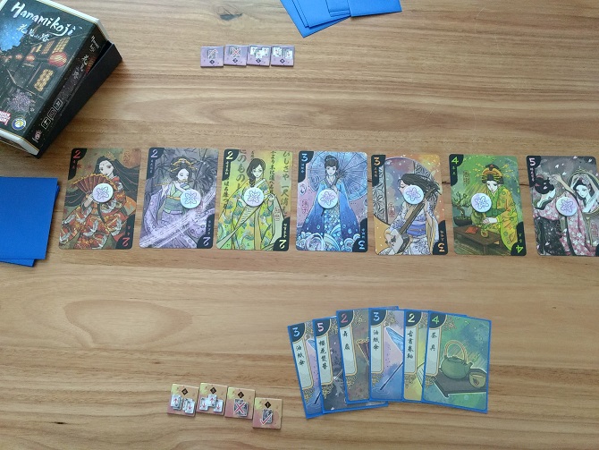 A game of Hanamikoji is set up and ready to play. Seven Geisha cards in the centre with a token placed upon each.