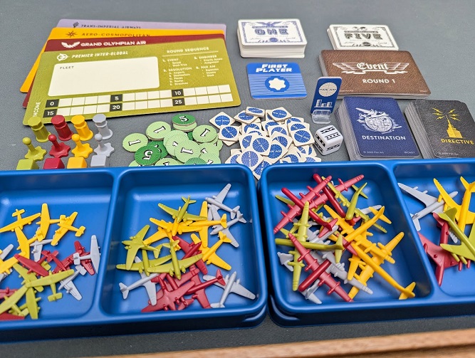 An overview of Pan Am board game pieces, including player mats, card decks, money tokens, and various colored plastic airplane miniatures in sorting trays.