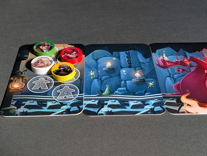 Four circular wooden player tokens representing dwarf characters gather on the mine exit space card. A fiery dragon card looms nearby at the end of the mine shaft track.